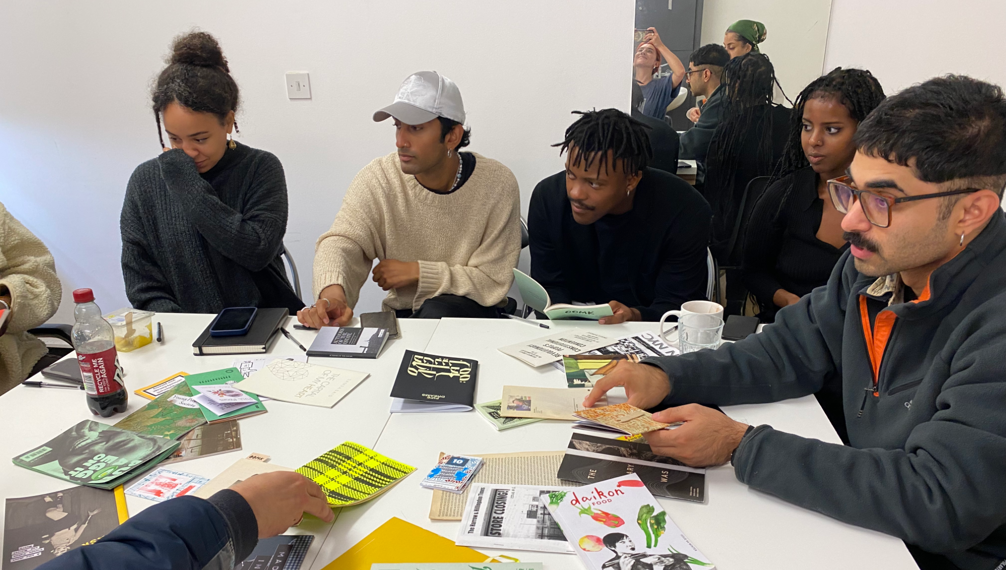 A diverse group of artists gathered around a table full of printed zines and pamphlets
